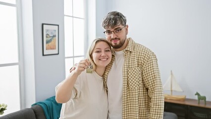 A smiling couple holding a key in a bright living room symbolizing new homeownership