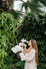Young woman stand in tropical garden and smell orchid flower. Young girl gardener taking care of...