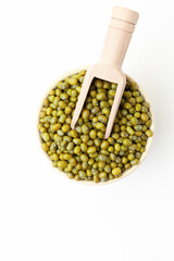Dry, green mung beans in bowl with wooden scoop on white background. Top view. Space for a text