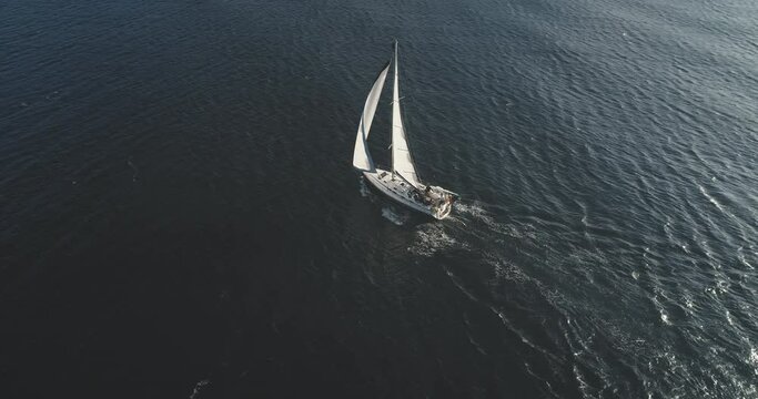 Top down slow motion of sailing yacht. Aerial sailboat regatta under sails at open sea. Racing yacht sail seascape. Luxury boat at summer cruise at Brodick harbor, Arran Island, Scotland, Europe