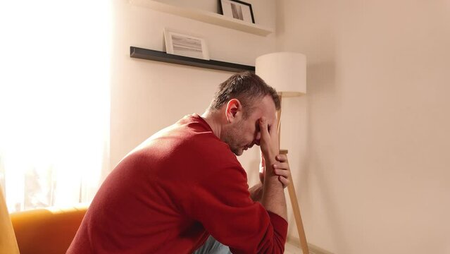 Man with headache sitting on a sofa at home.	
