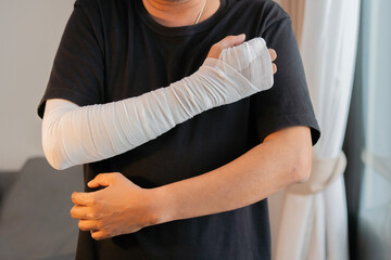 Young man with gauze bandage wrapped around his injured arms, hand and elbow at home.