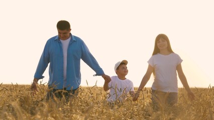 Smiling family man woman and boy son walking together on sunny dry wheat field. Happy mother father...