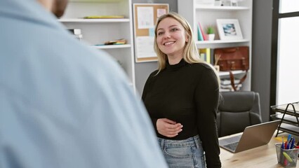A smiling woman converses with a colleague in a modern office, suggesting teamwork and a casual work environment.