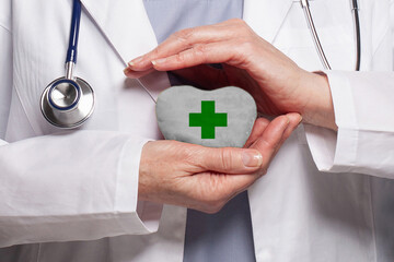 Green cross on white heart in medical worker hands. Healthcare, charity, insurance, medicine and veterinary concept