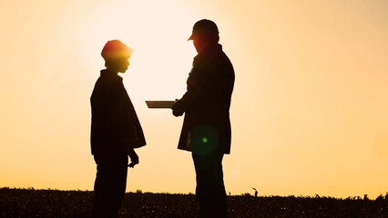 Silhouette man and woman farmer agronomist talking at sunset sunrise corn field. Agricultural work...
