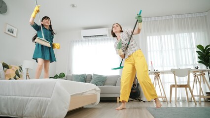 Caucasian mom and asian child doing housework together and dancing to music. Attractive mother and...