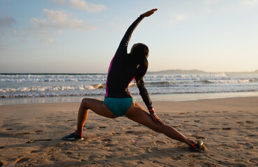 Woman surfer warming up on sunset beach - obrazy, fototapety, plakaty