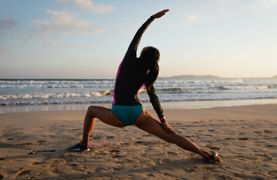 Woman surfer warming up on sunset beach