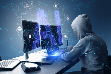 Side view of hacker in hoodie using computers at desk with glowing blue AI hologram on blurry...