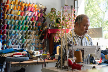 Latino man sewing in his clothing and sewing store - obrazy, fototapety, plakaty