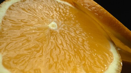A macrography capture of an orange slice, placed against a sleek, isolated black backdrop, unfolds...