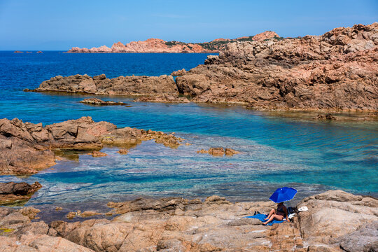 Woman under a sun umbrella on a rocky beach