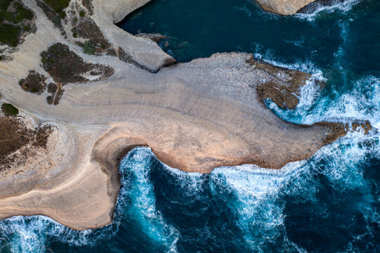 Waves crashing on white rock cliff drone aerial above view