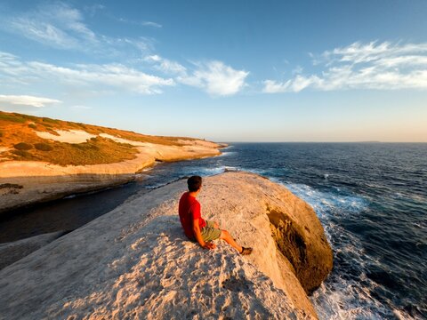 Back view of man sitting on white rock sea cliffs landscape