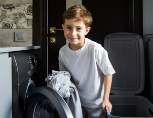 Boy putting laundry into washing machine at home.