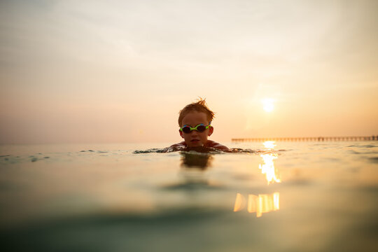 Child in goggles enjoys serene ocean swim at sunset