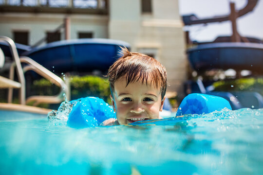 Cheerful child splashing in sunlit pool in front of water slides