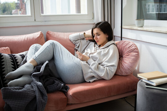 Young woman lying on coach in comfy clothes and scrolling on the phone