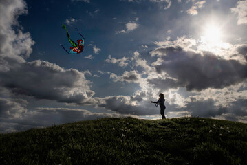 Young girl flying colorful kite on hill under bright sky
