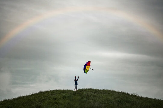 Young girl throwing rainbow umbrella in cloudy rainstorm