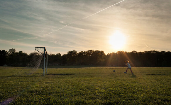 Young girl kicking ball into soccer goal in green field
