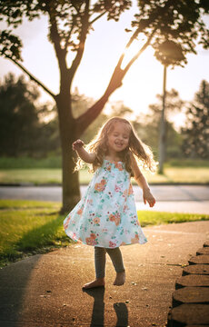 Beautiful happy little girl with long curls dancing outdoors in summer