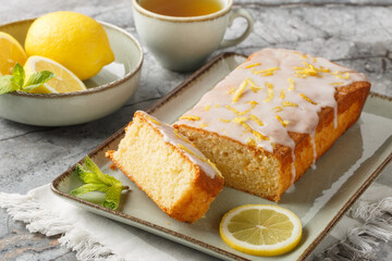 Lemon drizzle cake with lemon zest and icing is a classic British tea-time treat closeup on the plate on the table. Horizontal