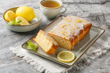 Homemade glazed lemon pound cake closeup on the plate served with tea on the table. Horizontal