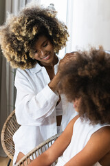Smiling young mother combing afro daughter
