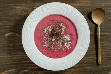 Sweet summer cherry soup in a white plate on a wooden background, closeup, top view. Hungarian cold red cherry soup with yogurt or cream, sprinkled with grated chocolate, powdered sugar and hazelnuts - 793669189
