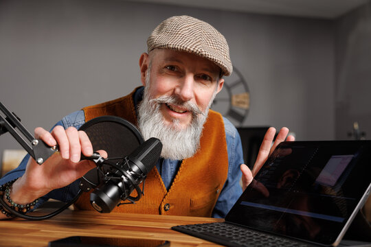 Studio podcast avec un micro et un ordinateur tablette et un homme souriant au look styl&eacute; et vintage avec une barbe hipster