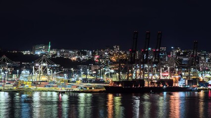 Auckland, New Zealand port nighttime time lapse with lights reflecting off the water as straddle carriers stack shipping containers