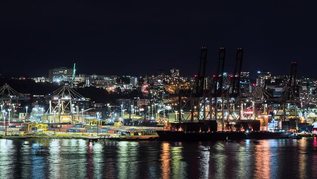 Auckland, New Zealand port nighttime time lapse with lights reflecting off the water as straddle carriers stack shipping containers