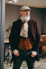 Portrait d'un homme original gentleman quinquagénaire senior hispter élégant et stylé avec un manteau un béret et un gilet dans un atelier créatif - 793679346