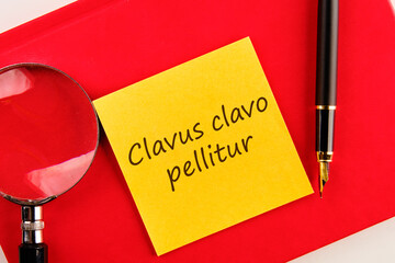Clavus clavo pellitur. The ancient Greek expression translates as, A wedge is knocked out with a wedge. on a yellow sticker on a red notebook - obrazy, fototapety, plakaty