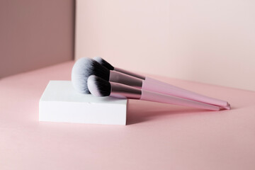Minimal set of foundation brushes, base concealer and powder on the white podium at pink background - obrazy, fototapety, plakaty