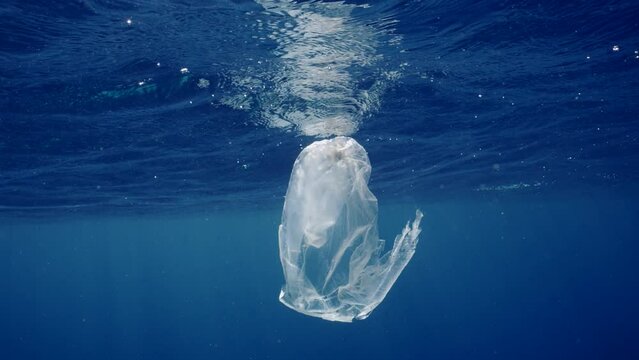 Plastic bag floating under storm waves inside blue Ocean, Slow motion. Environmental Issue underwater plastic pollution. An old torn transparent plastic bag floats underwater in blue water 