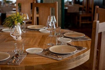 The interior of the restaurant is decorated in warm beige pastel shades with soft natural light. The table is set with clean glassware, glasses, a vase with flowers of yellow mimosa or silver acacia.