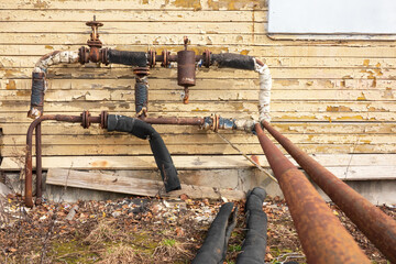 Old rusty heating system pipes on the wall of an abandoned wooden house with peeling yellow paint....