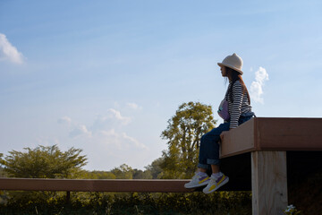 Asian girl sitting on a wooden bridge on a forest landscape background with sky.