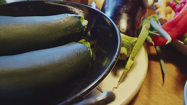 Close up of two whole fresh zucchini in a metal bowl on a wooden table. Also known as baby marrow, courgette, summer squash. Various other vegetables in the background. Kitchen interior. 