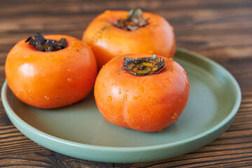 Ripe persimmon on a plate on a wooden background.