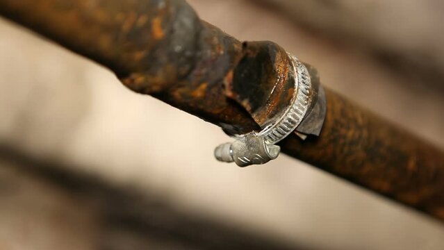 Metal clamp with rubber gasket on an old rusty water pipe. The water pipe in the basement is dripping.