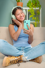 Beautiful woman with headphones listening to music on sofa happy shopping online with cell phone to...