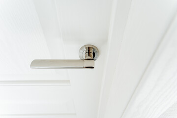 Metal handle on white door, shiny silver handle, stylish fittings in the interior.