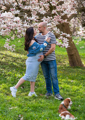 A man tenderly hugs his pregnant wife. The woman is wearing a blue dress. Couple man and pregnant woman near magnolia flowers