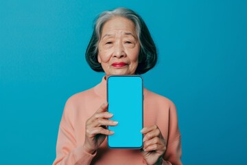 Display mockup asian woman in her 60s holding an smartphone with a fully blue screen