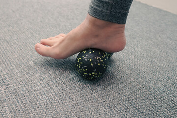 Massaging foot with a relaxing roll. Woman massaging foot with massage ball. Myofascial relaxation of foot muscles. Preventing foot fatigue
