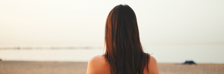 Beautiful brown-haired woman with long hair looks at the sea, Panorama, Back view